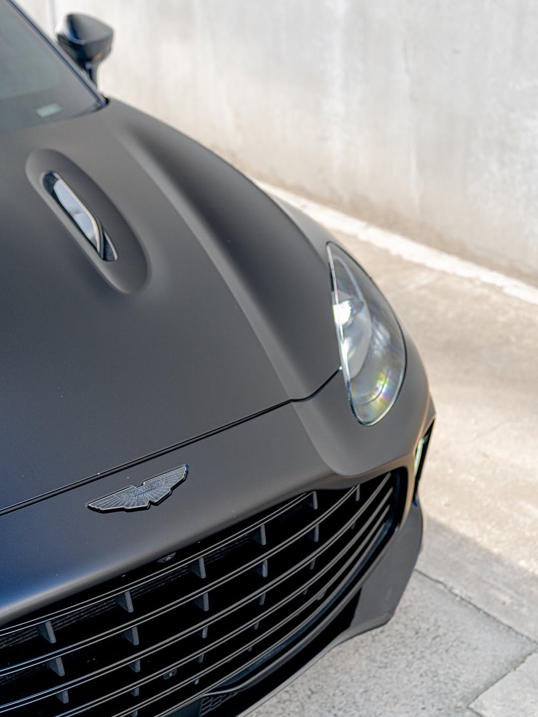 Silver luxury sedan protected with paint protection film against a concrete wall.